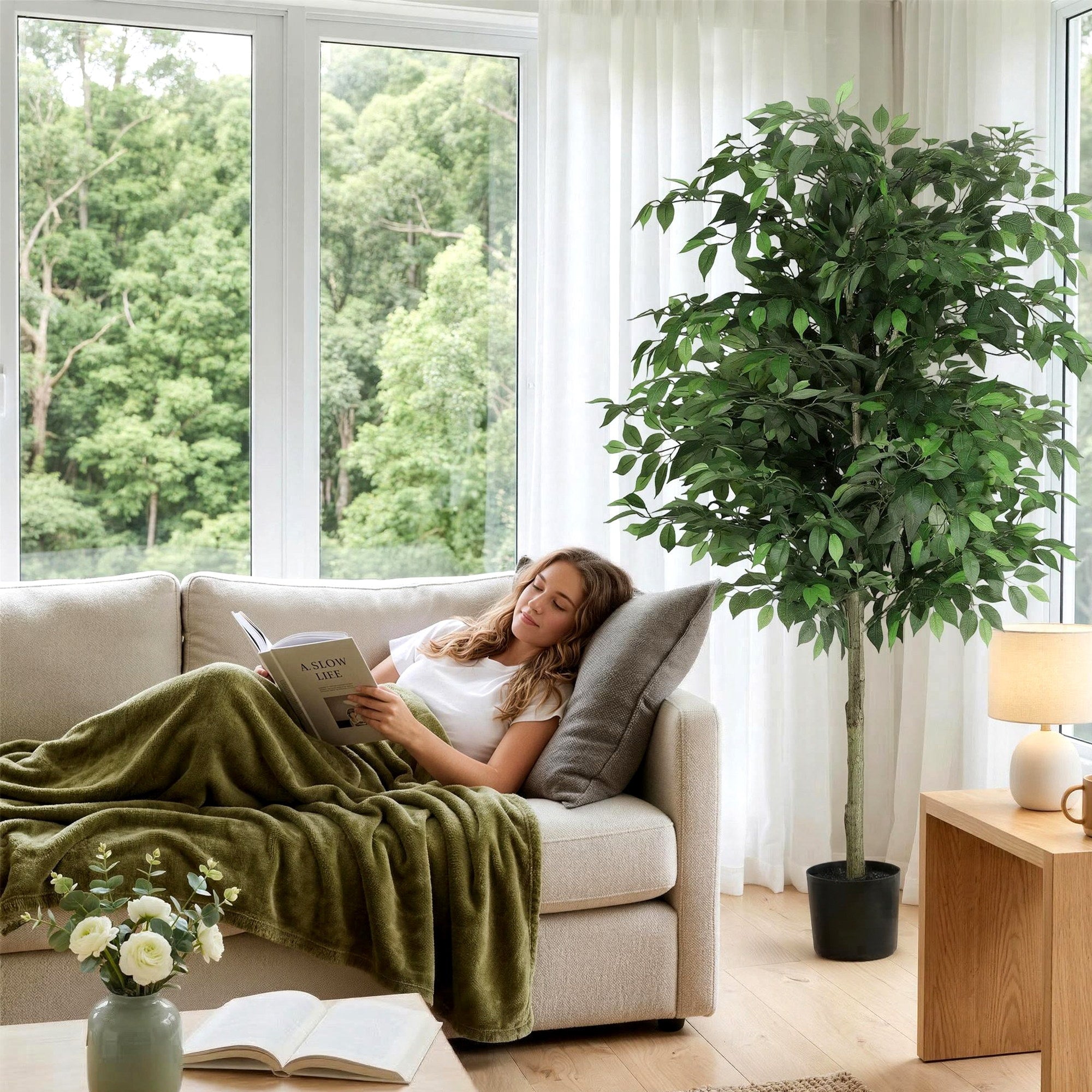 Woman reading a book on a couch in a bright living room with a large window and indoor plant.